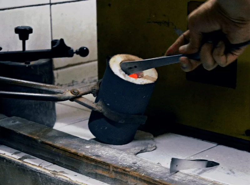 A crucible of molten metal being handled with tongs