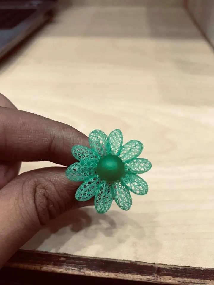 A green resin model of a flower ring held between two fingers