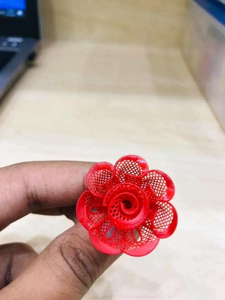 A red resin model of a flower ring held between two fingers